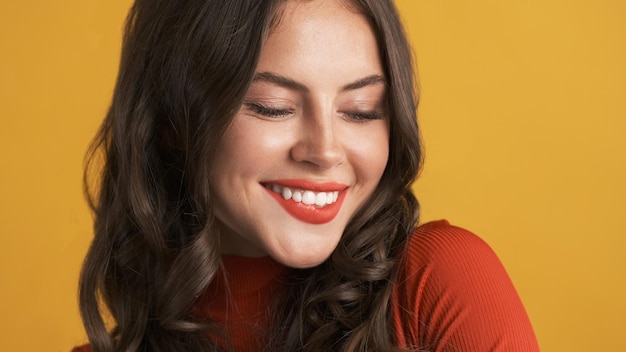 Close up charmante fille brune aux lèvres rouges souriant joyeusement à la caméra sur fond coloré