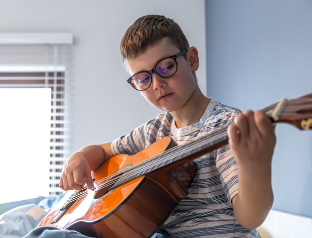 Close up cute boy avec des lunettes apprend à jouer de la guitare classique à la maison.