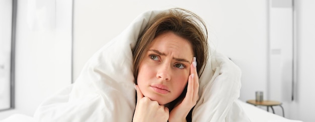 Photo gratuite close-up d'une femme se sentant mal à la maison allongée dans le lit sous des couvertures blanches et fronçant les sourcils touchant