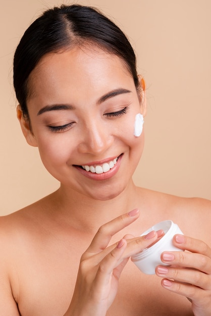 Close-up heureuse femme brune avec une crème pour le visage