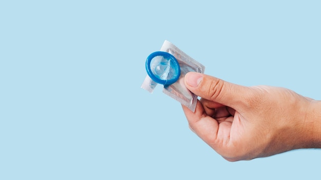 Close-up main tenant le préservatif avec fond bleu