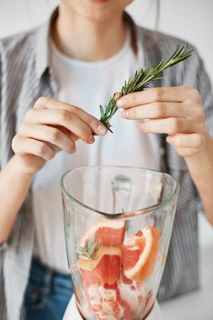 Close up of girl blending smoothie sain de pamplemousse detox ajoutant le romarin.