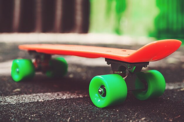 Close up orange penny skateboard sur l'asphalte derrière le mur vert