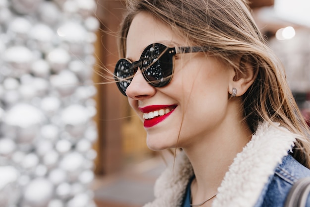 Close-up portrait de beau modèle féminin avec des lèvres rouges posant sur la rue. Photo extérieure de joyeuse fille blanche exprimant de bonnes émotions.