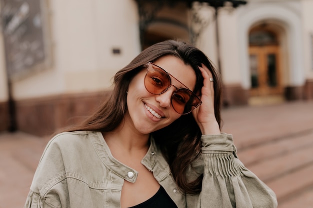 Close up portrait extérieur de charmante jolie femme portant des lunettes de soleil souriant et marchant sur la ville de printemps