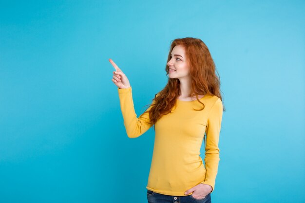 Close up Portrait jeune belle fille sexy redhair heureuse avec quelque chose et pointer le doigt. Blue Pastel Background. Espace de copie.