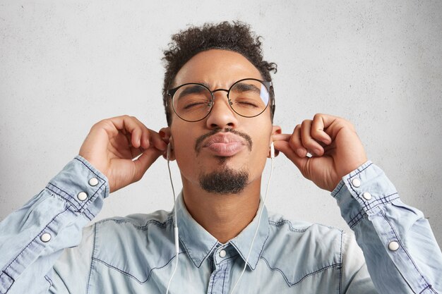 Close up portrait of Afro American man avec moustache et barbe porte chemise en jean et grosses lunettes rondes,