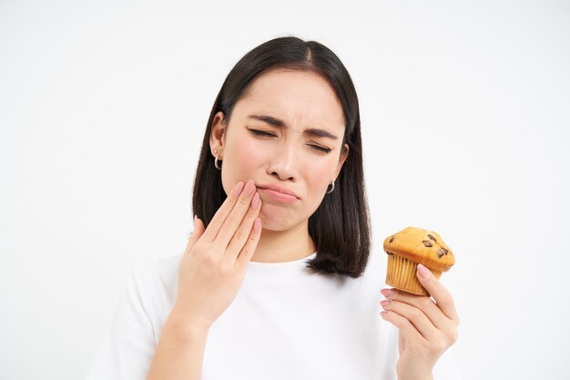 Close up portrait of asian woman with toothcahe regarde cupcake dessert trop sucré ne peut pas manger blanc ba