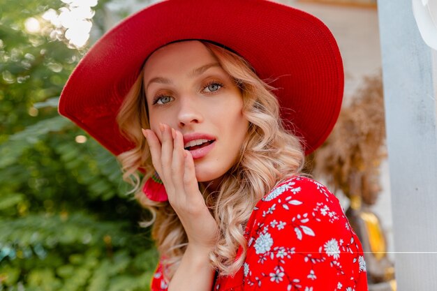 Close-up portrait of attractive blonde élégante femme souriante en chapeau rouge paille et chemisier tenue de mode d'été avec sourire sensuel