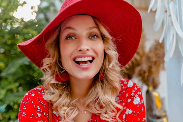 Close-up portrait of attractive blonde élégante femme souriante en chapeau rouge paille et chemisier tenue de mode d'été avec sourire