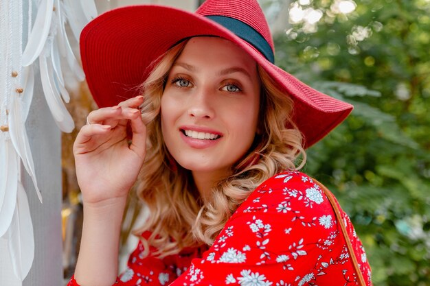 Close-up portrait of attractive blonde élégante femme souriante en chapeau rouge paille et chemisier tenue de mode d'été avec sourire