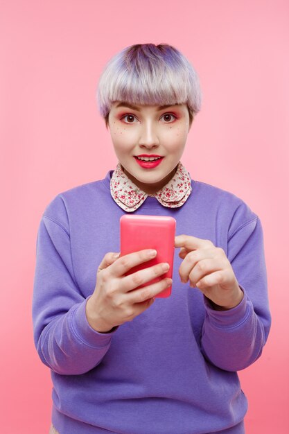 Close-up portrait of beautiful dollish girl with short light light hair wearing lilac sweater making selfie over pink wall