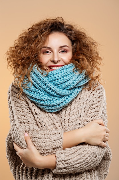 Photo gratuite close up portrait of cheerful smiling beautiful brunette curly girl in pull en tricot et cache-cou gris sur mur beige