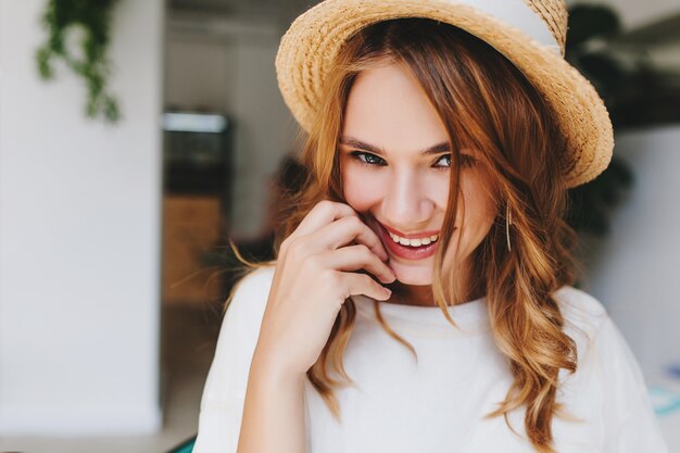 Close-up portrait of excité fille avec une coiffure élégante souriant et timide touchant le visage avec la main