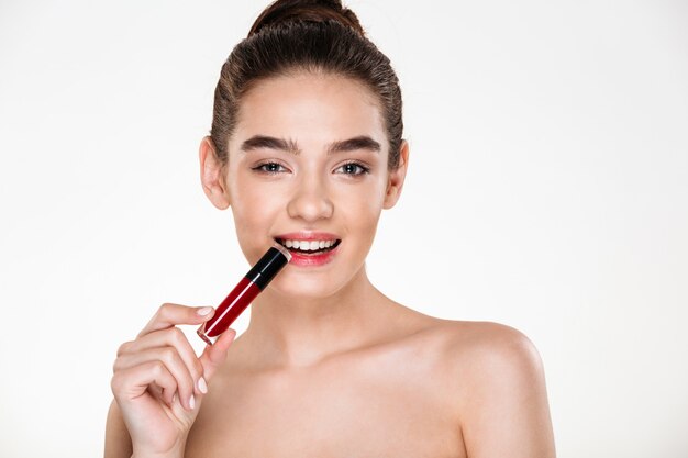 Close up portrait of flirting brunette woman with hair in bun holding lipstick in mouth looking