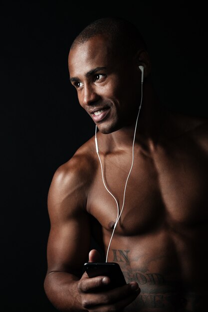 Close-up portrait of happy afro american sports man holding phone in hand tout en écoutant de la musique