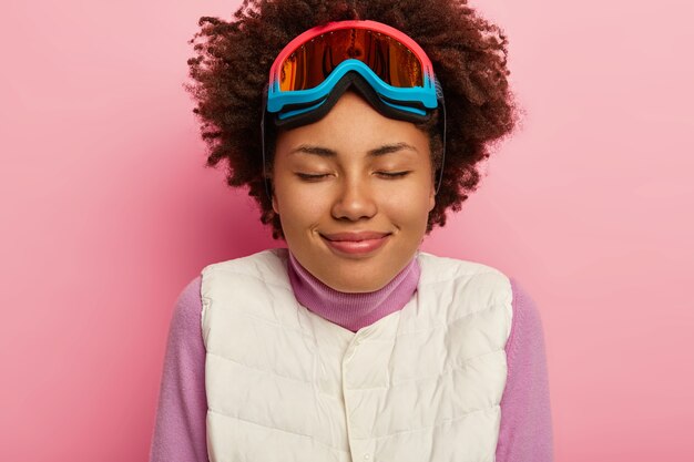 Close up portrait of happy skieur pose en gilet blanc, lunettes de snowboard, a une coiffure frisée