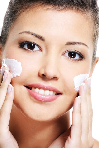 Close-up portrait of a happy young woman face avec une crème cosmétique sur la joue