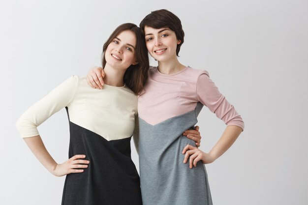 Close up portrait of joyful lesbian couple hugging étreignant, tenant la main sur la taille, posant pour la photo dans des tenues assorties.