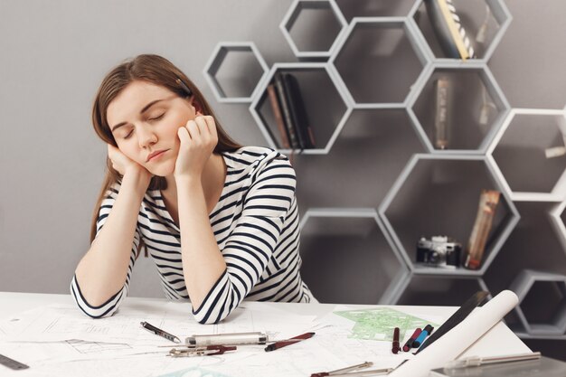 Close up portrait of sleepy charmant jeune ingénieur freelance européen fille s'endormir sur le lieu de travail pendant les préparatifs pour rencontrer le chef d'équipe pour parler des erreurs de travail
