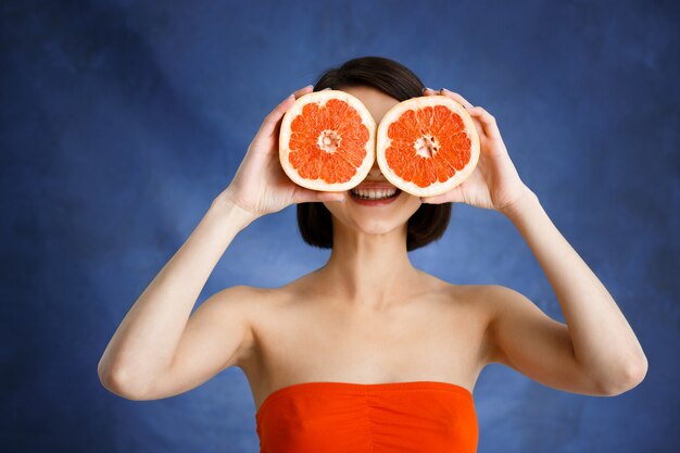 Close up portrait of tender young woman holding cut orange sur mur bleu