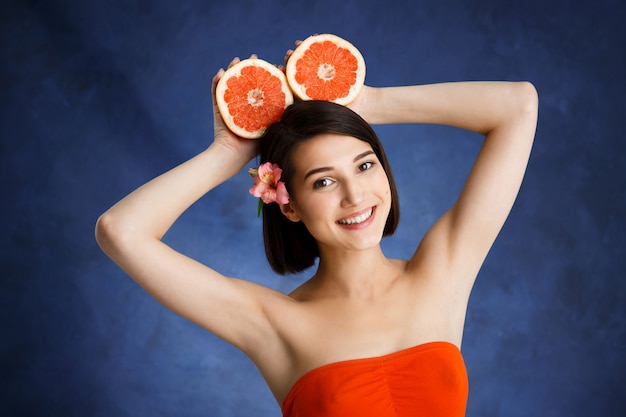 Close up portrait of tender young woman holding cut orange sur mur bleu