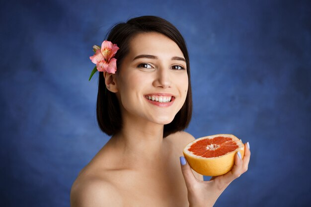 Close up portrait of tender young woman holding cut orange sur mur bleu