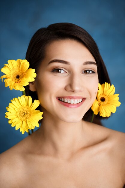 Close up portrait of tender young woman with yellow flowers over blue wall