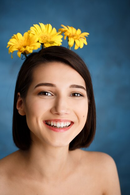 Close up portrait of tender young woman with yellow flowers over blue wall