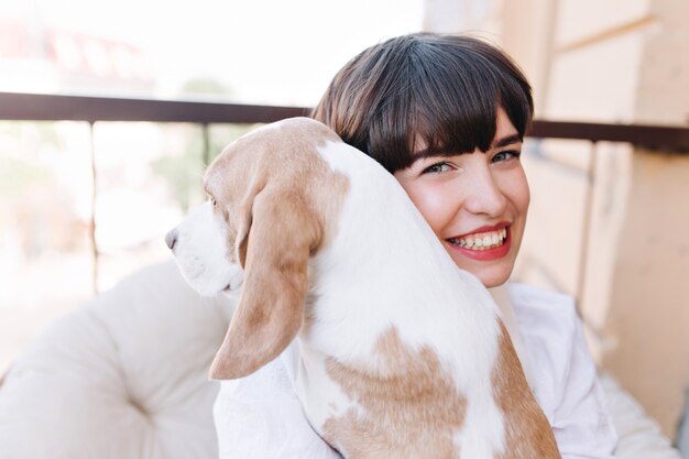 Close-up portrait en plein air de jeune fille souriante aux cheveux brun foncé tenant un chien beagle