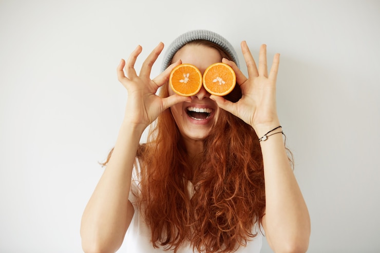 Photo gratuit close up portrait en studio de jeune femme souriante tenant les moitiés d'oranges à ses yeux