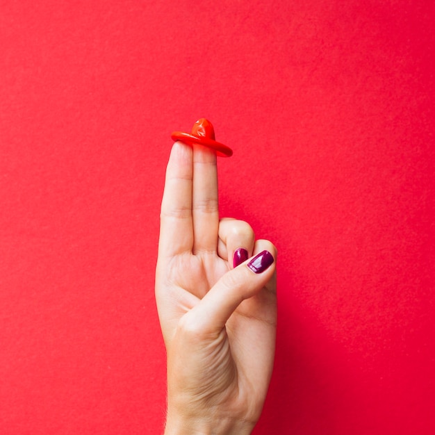 Close-up préservatif rouge sur les doigts de la femme