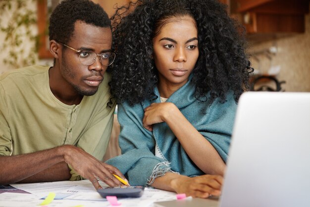 Close-up shot candide de jeune couple à la peau sombre assis devant un ordinateur portable ouvert