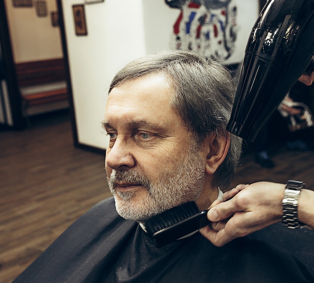 Close-up side view portrait of handsome senior barbu caucasian man getting beard grooming in modern barbershop.
