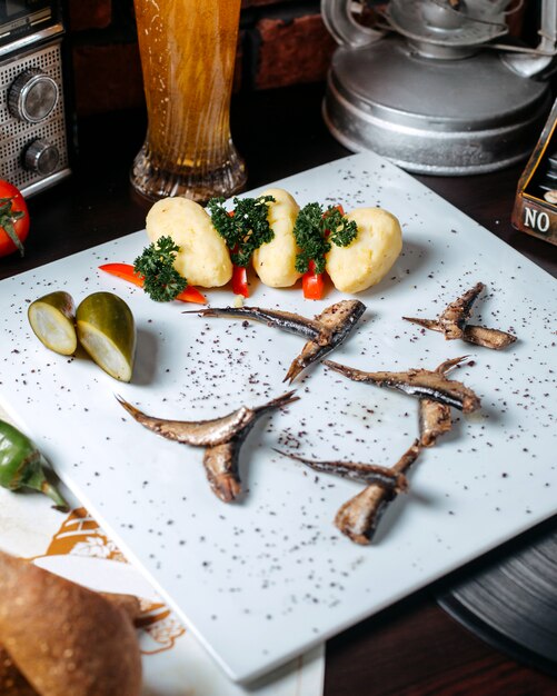 Close up de sprat épicé poêlé aux concombres marinés et pommes de terre bouillies sur fond blanc