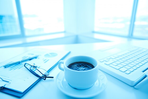 Close-up de la tasse de café avec un ordinateur portable et des lunettes