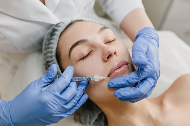 Closeup portrait de belle femme au cours de la thérapie de cosmétologie dans un salon de beauté. Botox, lèvres, injection, procédures professionnelles, levage, rajeunissement, appareils modernes, soins de santé