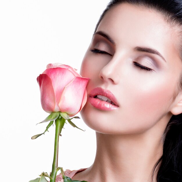 Closeup portrait de belle femme sensuelle avec rose rose sur mur blanc.