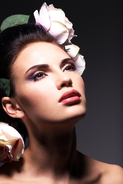 Closeup portrait de belle jeune femme avec des fleurs roses dans les cheveux - sur fond gris