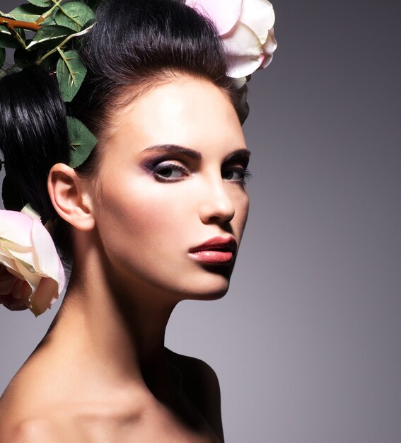 Closeup portrait de belle jeune femme avec des fleurs roses dans les cheveux - sur fond gris