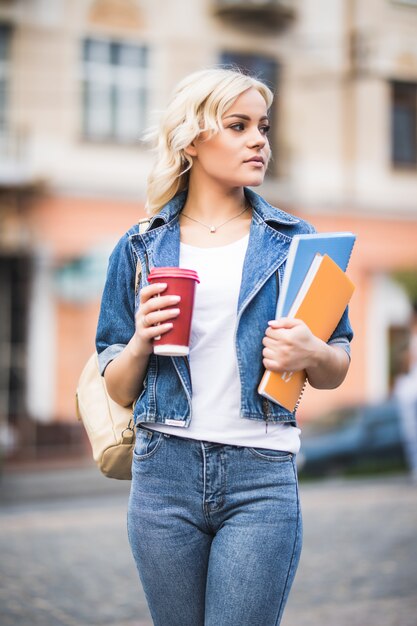 Closeup portrait d'étudiant fille blonde souriante avec beaucoup de cahiers habillés en jeans