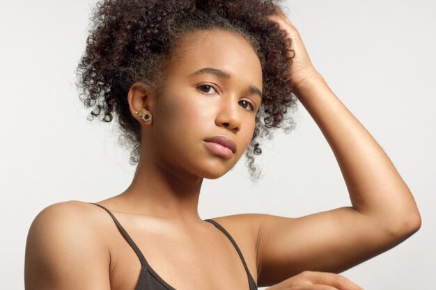 Closeup portrait de jeune mannequin métisse aux cheveux bouclés en studio avec un maquillage neutre naturel touche ses cheveux