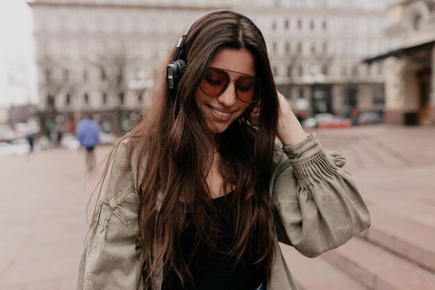 Closeup portrait de joyeuse femme souriante se détendre avec de la musique dans la ville Tir en plein air du modèle féminin souriant dans les écouteurs, passer du temps le week-end