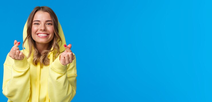 Photo gratuit closeup portrait of cute and silly blonde caucasian girl in yellow hoodie montrant korean heart gestur