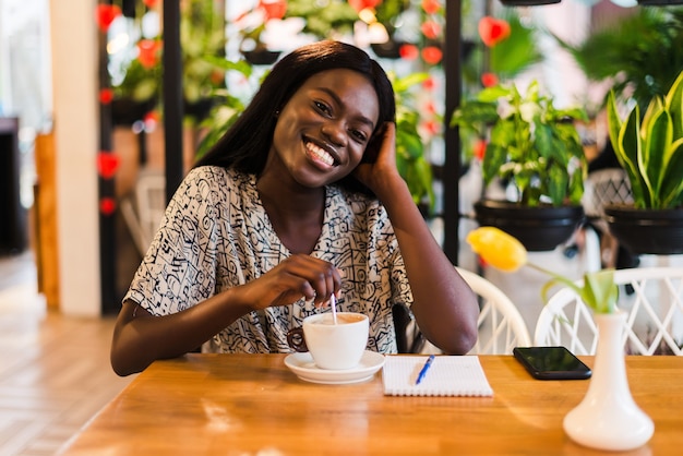 Closeup portrait of happy young black woman buvant du café au café