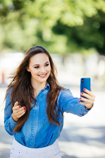 Closeup selfie-portrait étudiant de jolie fille à lunettes de soleil avec une coiffure longue et un sourire blanc comme neige en ville.