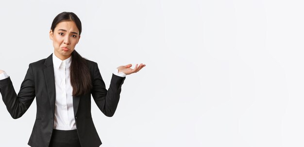 Clueless contrarié young asian female office worker manager en costume noir haussant les mains écartées si