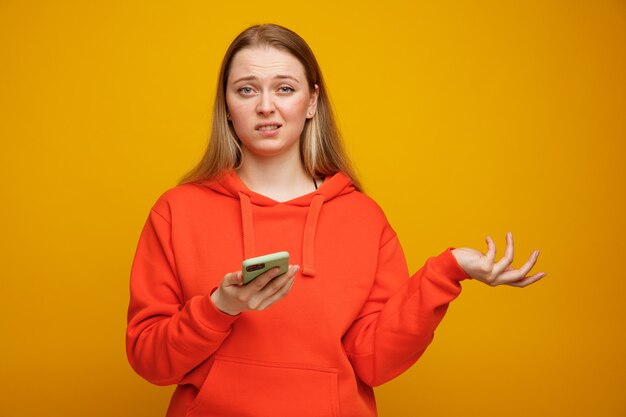 Clueless young blonde woman holding mobile phone montrant la main vide