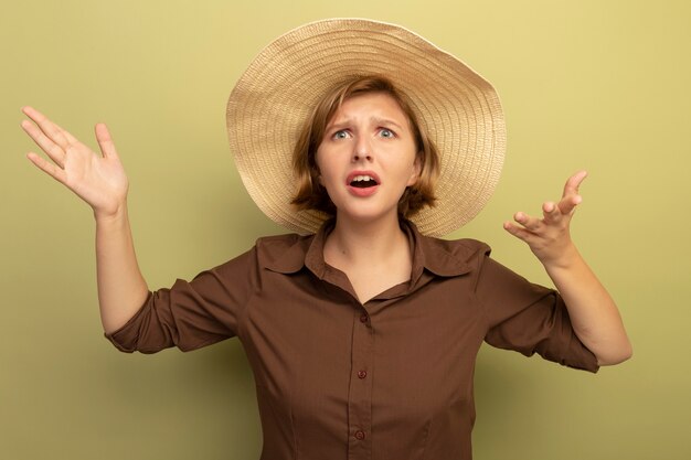 Clueless young blonde woman wearing beach hat à droite montrant les mains vides