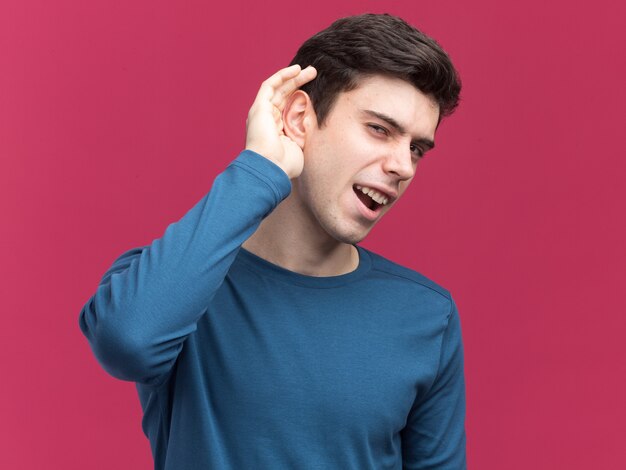 Clueless young brunette caucasian boy tient la main derrière l'oreille en essayant de se diriger sur rose